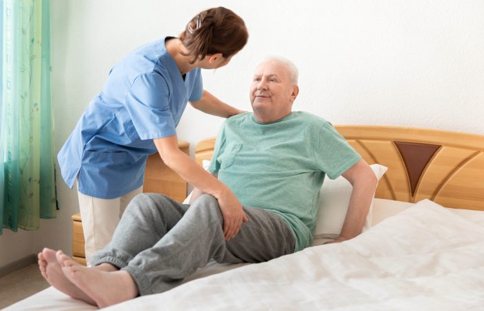 Nursing home â€“ home caregiver helping an elderly man out of bed