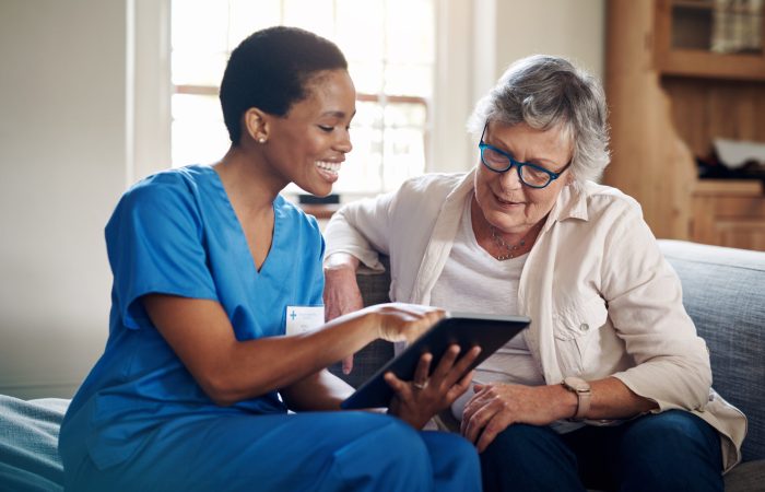 Shot of a senior woman using a digital tablet with a nurse on the sofa at home