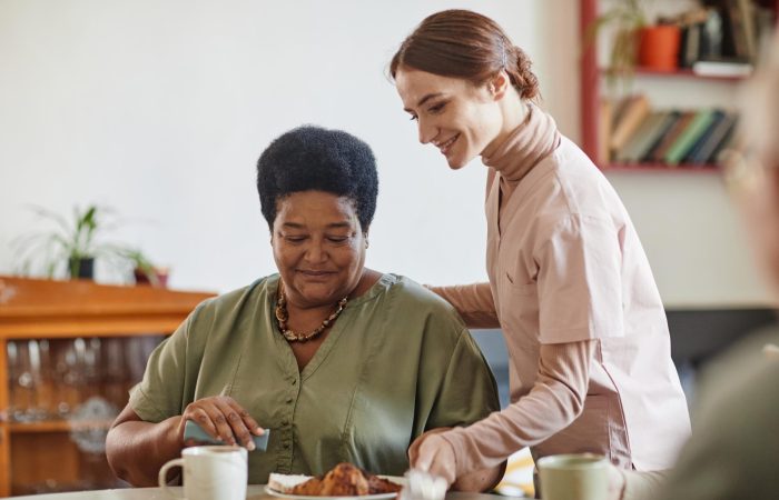 Portrait of smiling young woman caring for senior African-American lady in nursing home, copy space