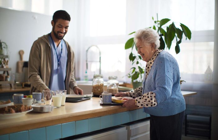 A young caregiver serving breakfast to elderly woman in nursing home care center.